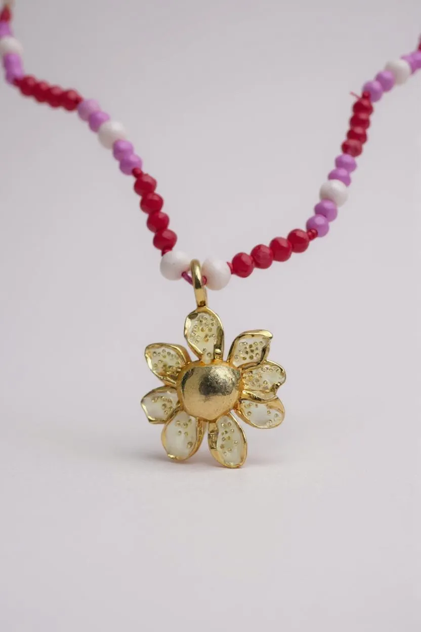 Daisy necklace in gold-plated bronze with hand-painted pendant and pink and fuchsia crystals, on white background.