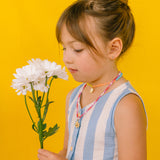 Girl in a light blue dress wearing the handmade Daisy Necklace with golden pendant and pink crystal chain.