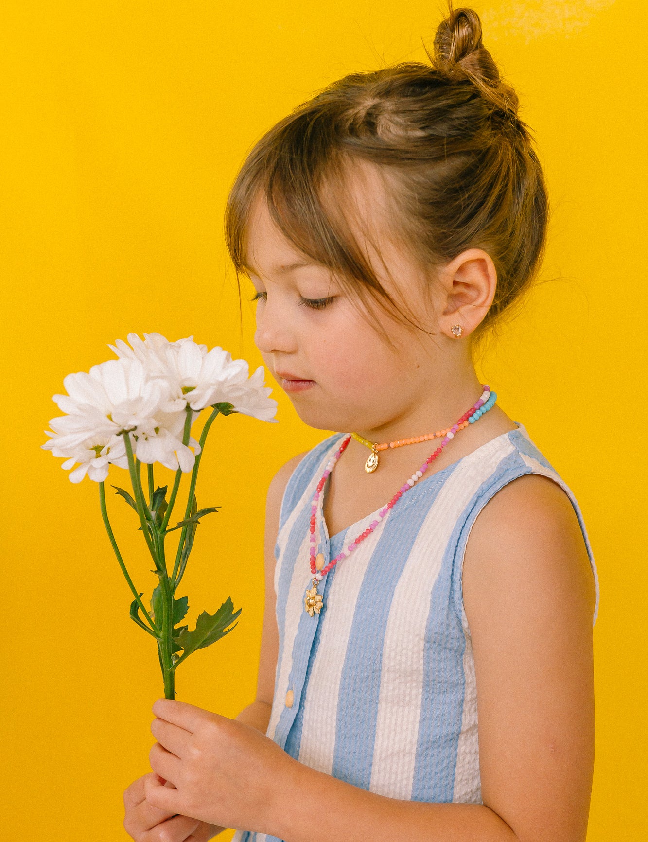 Girl in a light blue dress wearing the handmade Daisy Necklace with golden pendant and pink crystal chain.