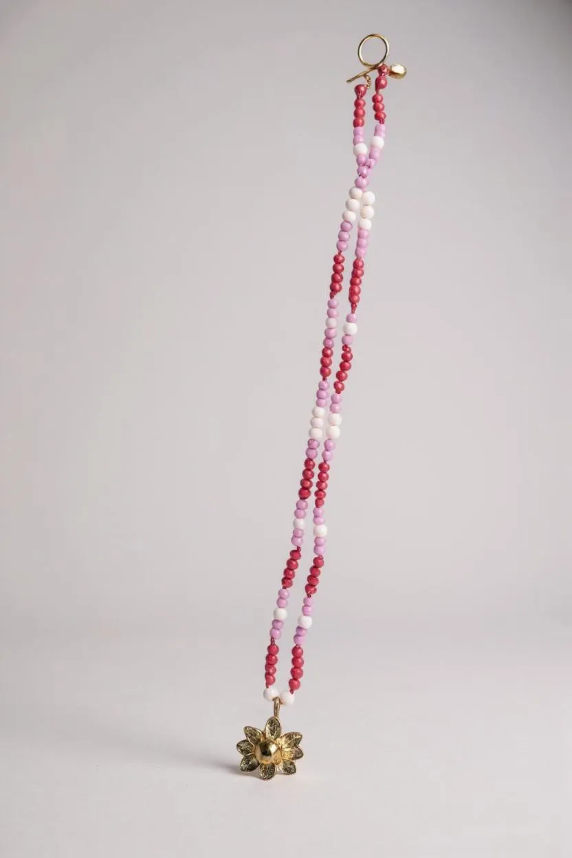 Daisy necklace displayed flat, with golden flower pendant and pink, fuchsia, and white crystal chain.