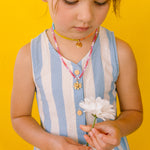Girl in a blue dress looking down while wearing the handmade Daisy Necklace with golden pendant.