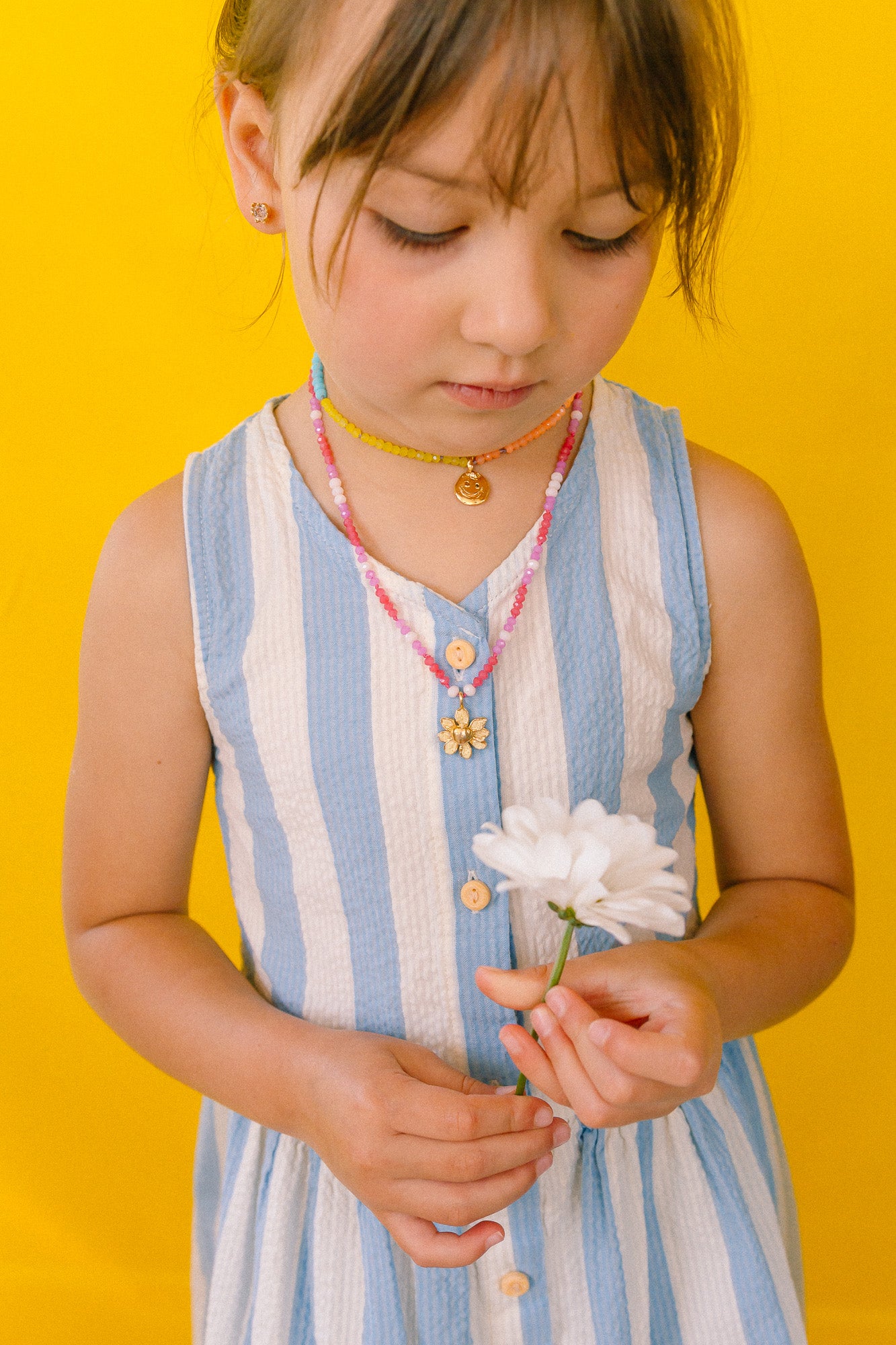 Girl in a blue dress looking down while wearing the handmade Daisy Necklace with golden pendant.