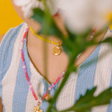 Close-up of the Margarita Necklace golden pendant surrounded by pink, white, and fuchsia crystals.