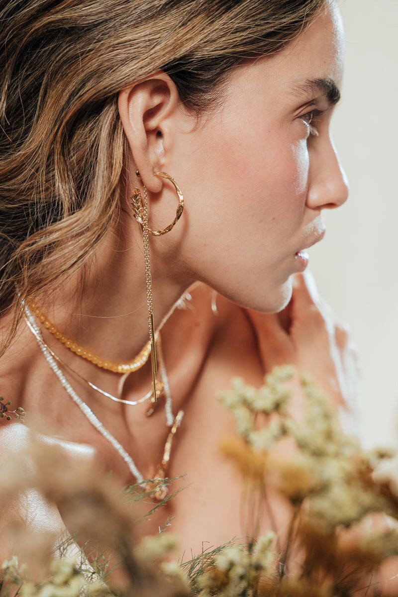 Model wearing Espiga hoops in a natural setting surrounded by foliage, highlighting the botanical and artisanal style of the jewelry.