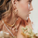 Model wearing Espiga hoops in a natural setting surrounded by foliage, highlighting the botanical and artisanal style of the jewelry.