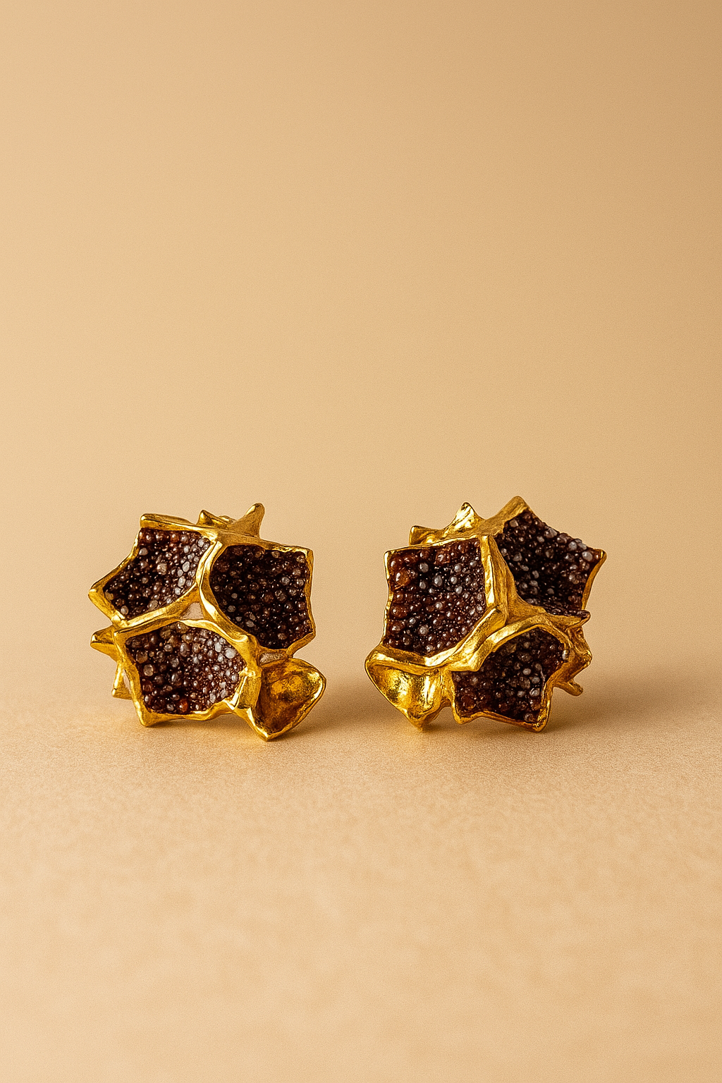  Close-up of a pair of Galaxea stud earrings in rust—gold-plated star-shaped earrings filled with clusters of rust-colored glass granules—on a warm beige background.