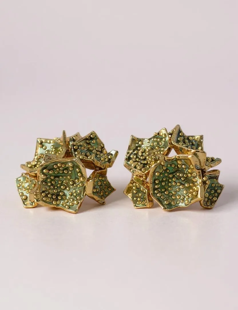 Pair of Galaxea stud earrings in sage—gold-plated floral-shaped earrings with clusters of sage-green glass granules—displayed on a pale pink background.