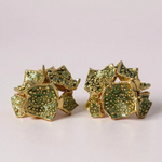 Pair of Galaxea stud earrings in sage—gold-plated floral-shaped earrings with clusters of sage-green glass granules—displayed on a pale pink background.