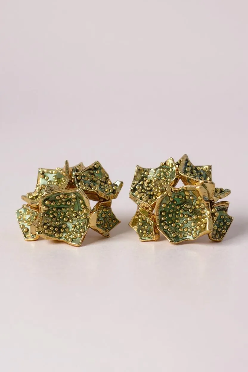 Pair of Galaxea stud earrings in sage—gold-plated floral-shaped earrings with clusters of sage-green glass granules—displayed on a pale pink background.