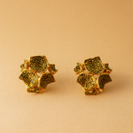 Two Galaxea sage stud earrings—gold-plated floral-shaped studs with sage-green glass granules—positioned side by side on a warm beige background.