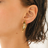 Close-up side view of a woman’s ear wearing the Mustard variant of the Lettuce Leaf Earring, hand-painted mustard-yellow with glass granulation on a gold-plated bronze setting, hair tucked behind ear against a neutral background.