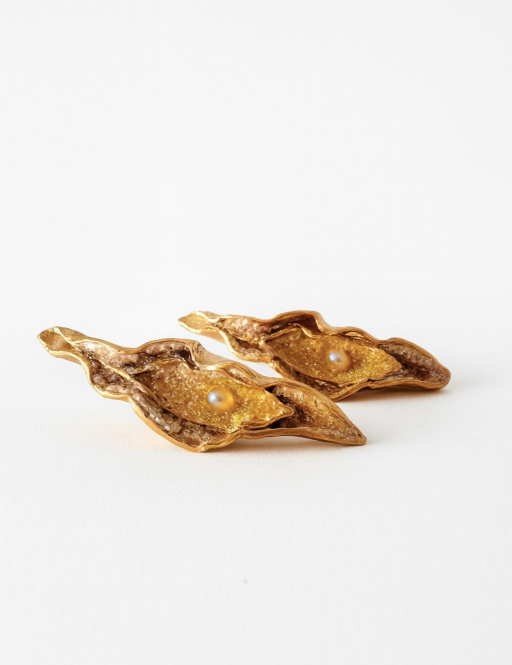 Flat lay of two Mustard variant Lettuce Leaf Earrings in gold-plated bronze, hand-painted in rust with glass granulation, placed on a white background.