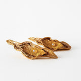 Flat lay of two Mustard variant Lettuce Leaf Earrings in gold-plated bronze, hand-painted in rust with glass granulation, placed on a white background.
