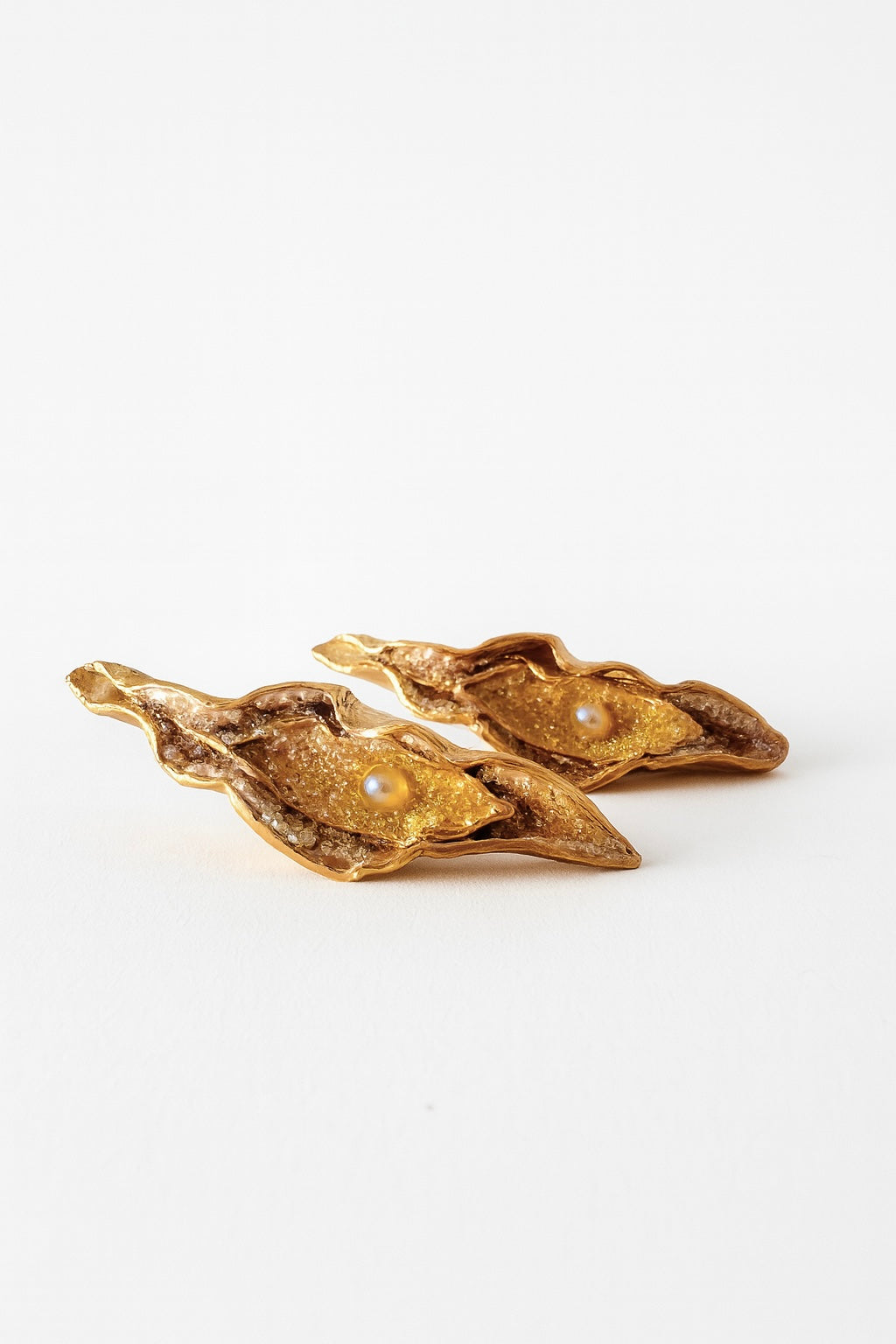 Flat lay of two Mustard variant Lettuce Leaf Earrings in gold-plated bronze, hand-painted in rust with glass granulation, placed on a white background.