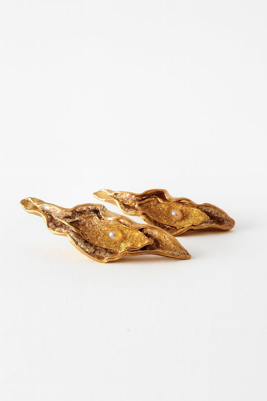 Flat lay of two Mustard variant Lettuce Leaf Earrings in gold-plated bronze, hand-painted in rust with glass granulation, placed on a white background.