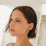 Portrait of a woman wearing the Mustard variant of the Lettuce Leaf Earrings, hand-painted in rust with glass granulation on a gold-plated bronze setting, posed against a light neutral background.