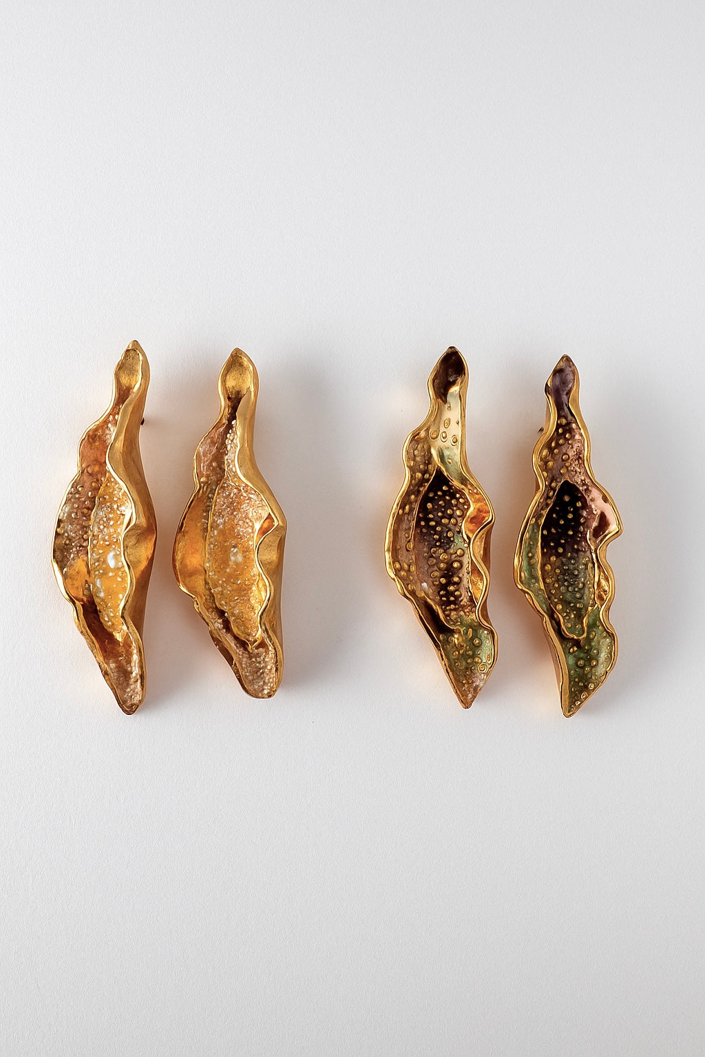 Flat lay of four Lettuce Leaf Earrings on a white background—two hand-painted mustard-yellow and two rust variant, all with glass granulation and gold-plated bronze settings.