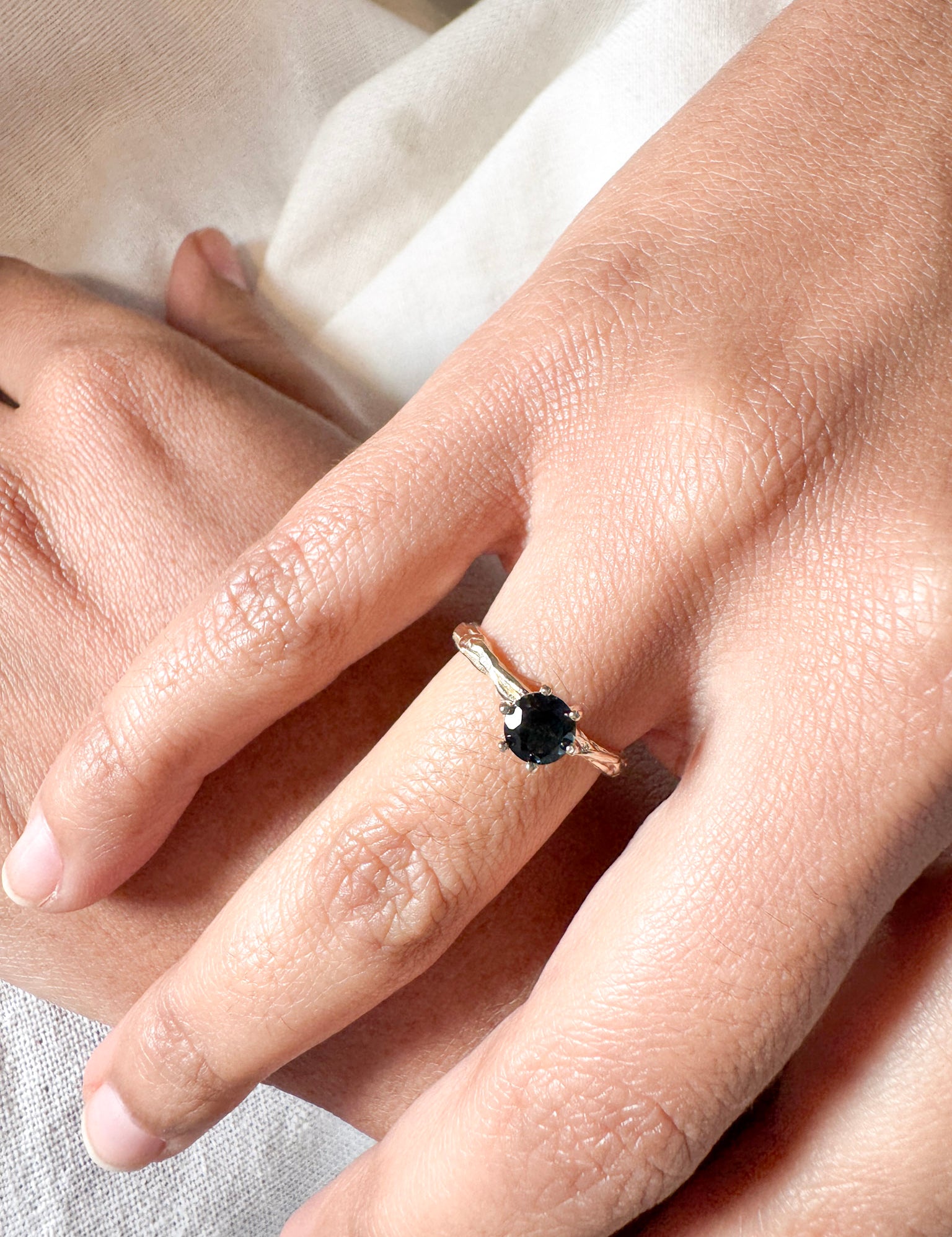 London blue topaz ring in 10k yellow gold worn on a hand, photographed over soft fabric.