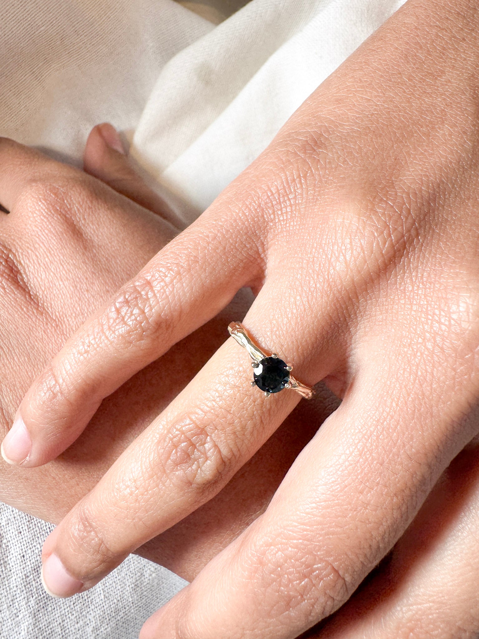 London blue topaz ring in 10k yellow gold worn on a hand, photographed over soft fabric.