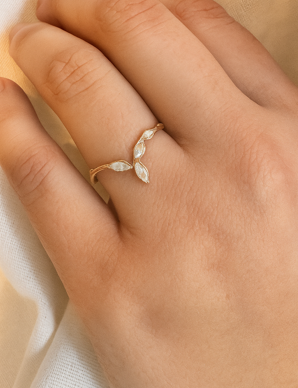 Rose gold Marqueza ring with zircons worn on a hand, photographed over soft fabric.