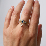 Montana sapphire and lab-grown diamond ring in 10k yellow gold worn on a hand, photographed against a light neutral background.