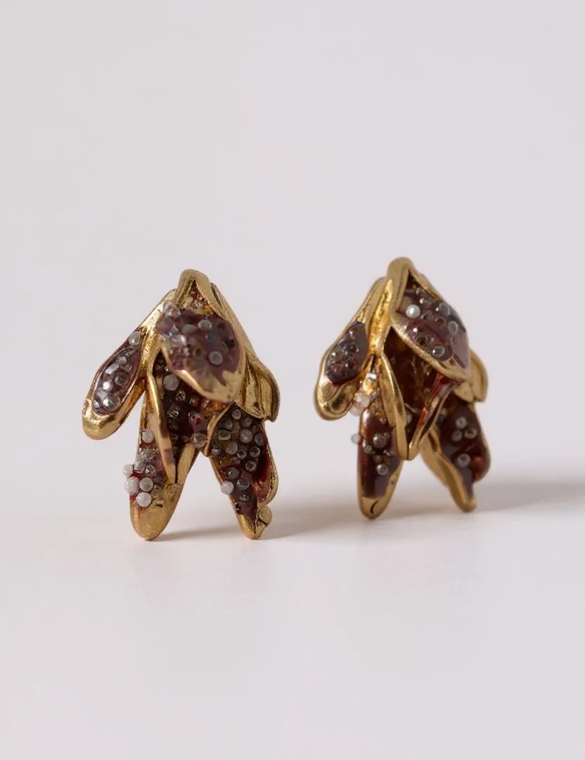 Pair of Topos Nebula Mini leaf-shaped stud earrings in gold-plated brass, hand-painted with rust paint and topped with glass granulation, displayed on a white background.
