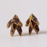Pair of Topos Nebula Mini leaf-shaped stud earrings in gold-plated brass, hand-painted with rust paint and topped with glass granulation, displayed on a white background.