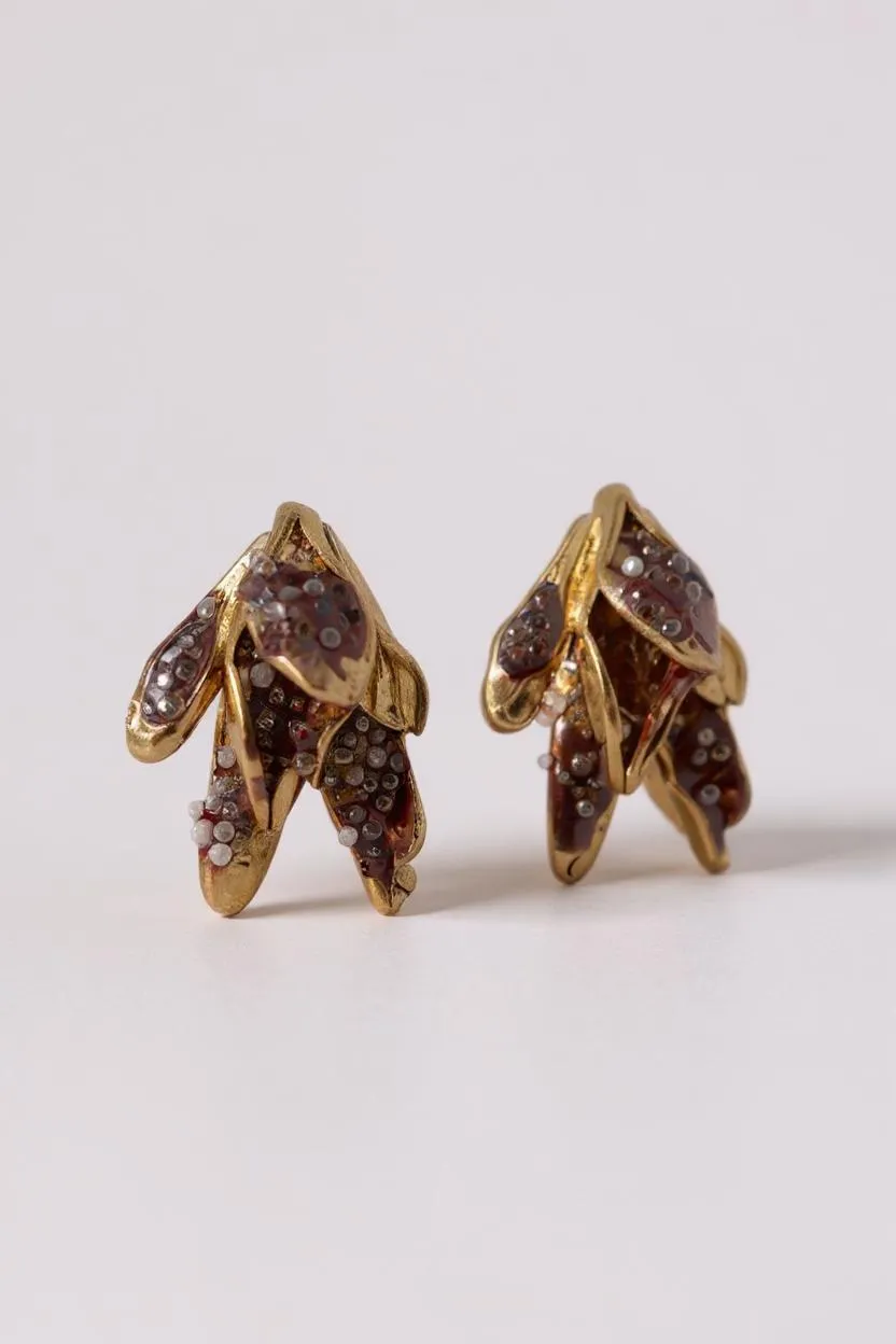 Pair of Topos Nebula Mini leaf-shaped stud earrings in gold-plated brass, hand-painted with rust paint and topped with glass granulation, displayed on a white background.