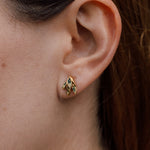 Close-up side view of a woman’s ear wearing a single Topos Nebula Mini stud earring in gold-plated brass, hand-painted with green  paint and glass granulation, her hair tucked behind her ear against a neutral backdrop.