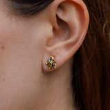 Close-up side view of a woman’s ear wearing a single Topos Nebula Mini stud earring in gold-plated brass, hand-painted with green  paint and glass granulation, her hair tucked behind her ear against a neutral backdrop.