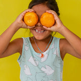 “Young girl in a mint sleeveless top holds two oranges over her eyes, smiling against a bright yellow background.