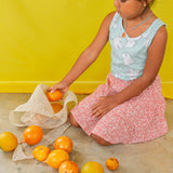 Child kneeling on the floor in a mint top and pastel skirt plays with oranges and wears the Orange Necklace.