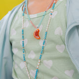 Close‑up of a child in a mint sleeveless top wearing the Orange Necklace, with the pendant resting near her chest against a yellow background