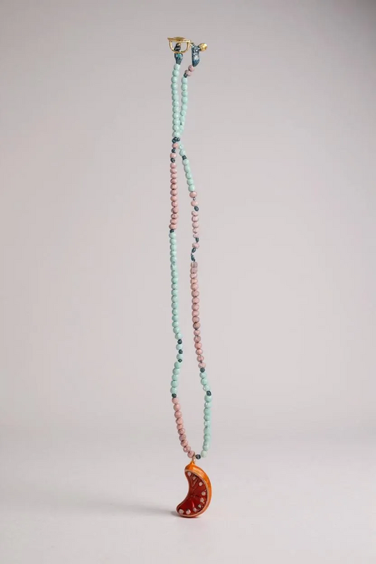 Orange Necklace laid out vertically on grey, showing its full strand of alternating mint-green and pink beads and the bright orange crescent moon pendant at the bottom