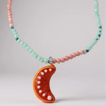 Close-up of the Orange Necklace pendant and beads, highlighting the glossy bright orange crescent moon charm decorated with tiny metal studs amid mint-green and pink beads