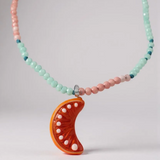 Close-up of the Orange Necklace pendant and beads, highlighting the glossy bright orange crescent moon charm decorated with tiny metal studs amid mint-green and pink beads