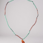 Orange Necklace arranged in a circular loop on a grey surface, emphasizing the pattern of mint-green and pink beads with the bright orange crescent pendant resting at the bottom.