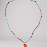 Orange Necklace arranged in a circular loop on a grey surface, emphasizing the pattern of mint-green and pink beads with the bright orange crescent pendant resting at the bottom.