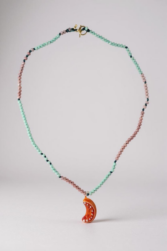 Orange Necklace arranged in a circular loop on a grey surface, emphasizing the pattern of mint-green and pink beads with the bright orange crescent pendant resting at the bottom.