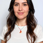 Portrait of a woman with long dark hair wearing a white shirt and the Orange Necklace, centered on her neckline against a white background.