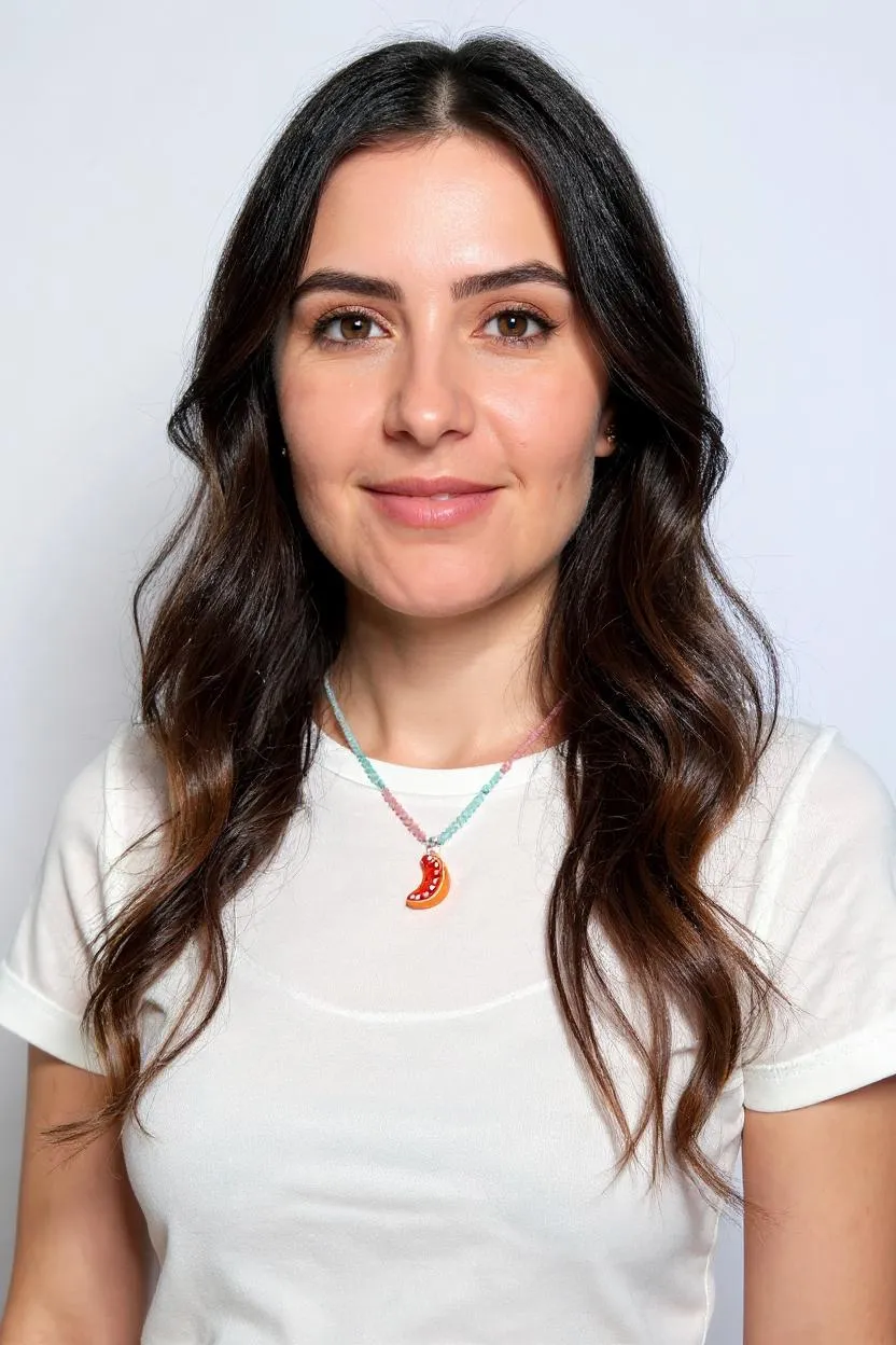 Portrait of a woman with long dark hair wearing a white shirt and the Orange Necklace, centered on her neckline against a white background.