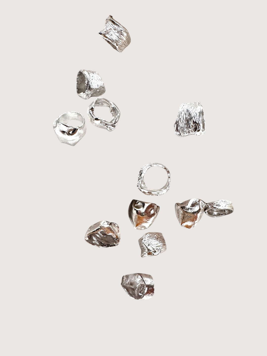 Collection of handcrafted silver rings with organic textures and irregular shapes, displayed on a neutral background