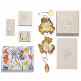 Collection of decorative items including a floral-patterned box, gold butterfly ornament, and 'Capa' branded boxes on a white background.
