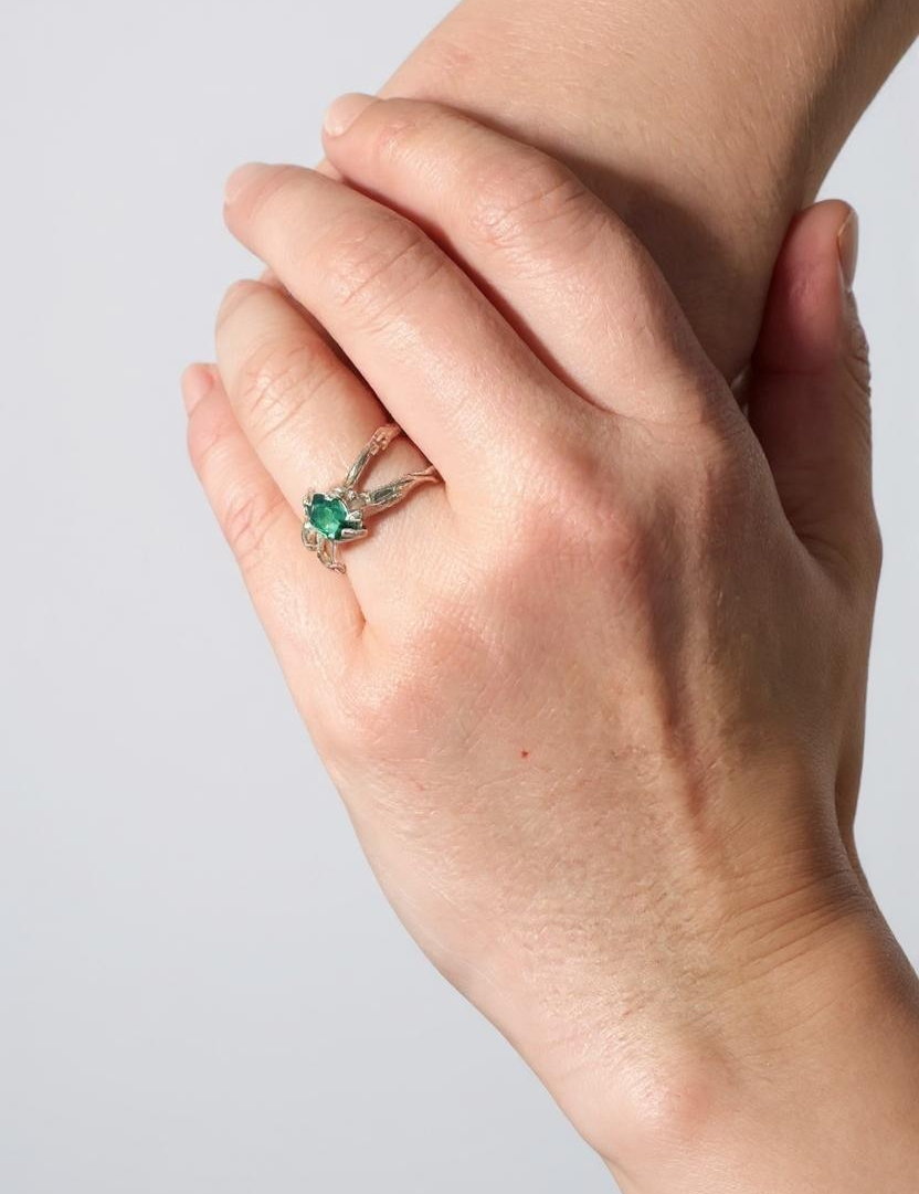 Lab-grown emerald sterling silver ring worn on a hand, photographed against a light grey wall.