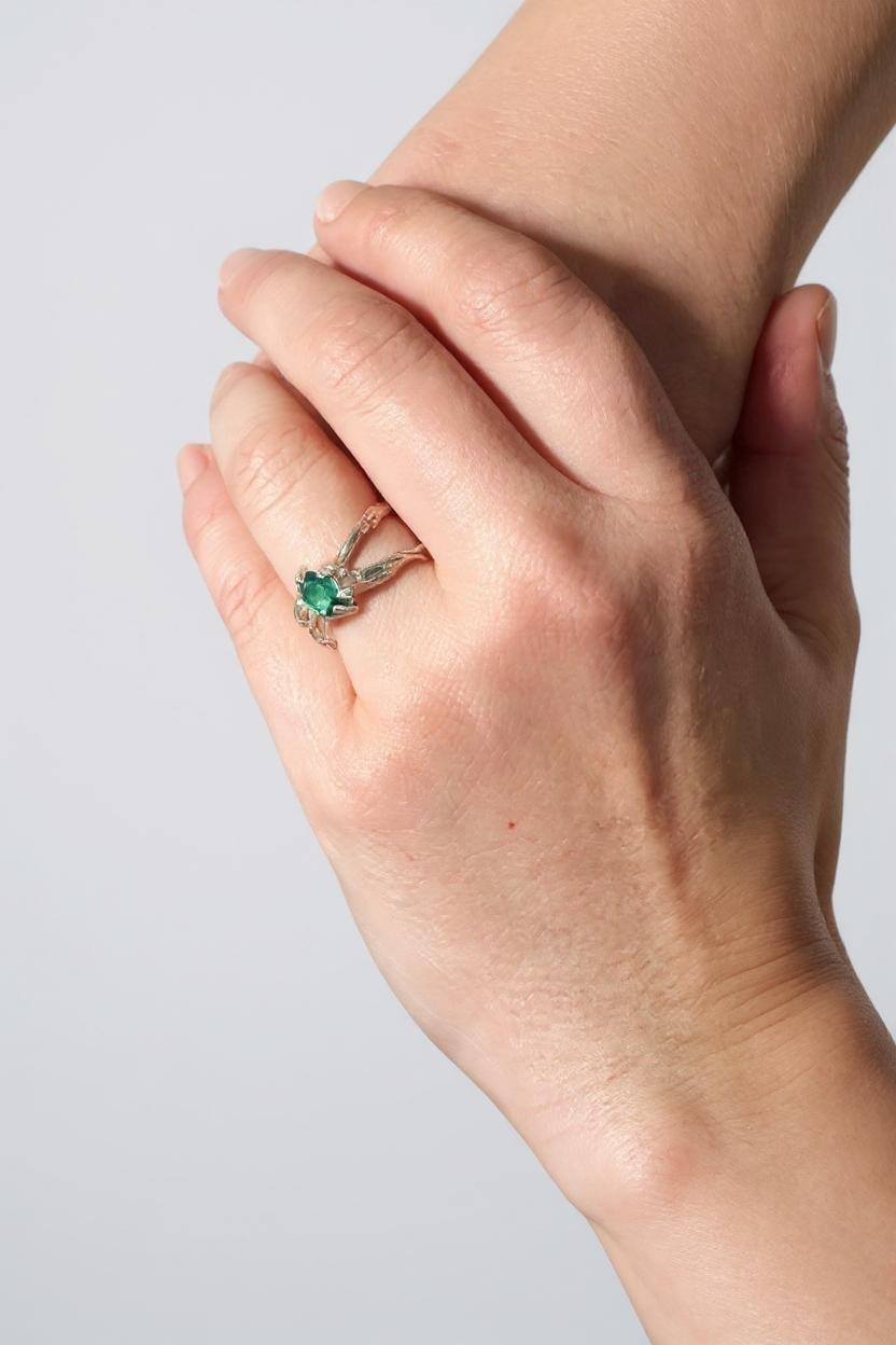 Lab-grown emerald sterling silver ring worn on a hand, photographed against a light grey wall.