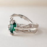 Front-angled view of the sterling silver ring with a vivid green lab-grown emerald, placed on a white surface.