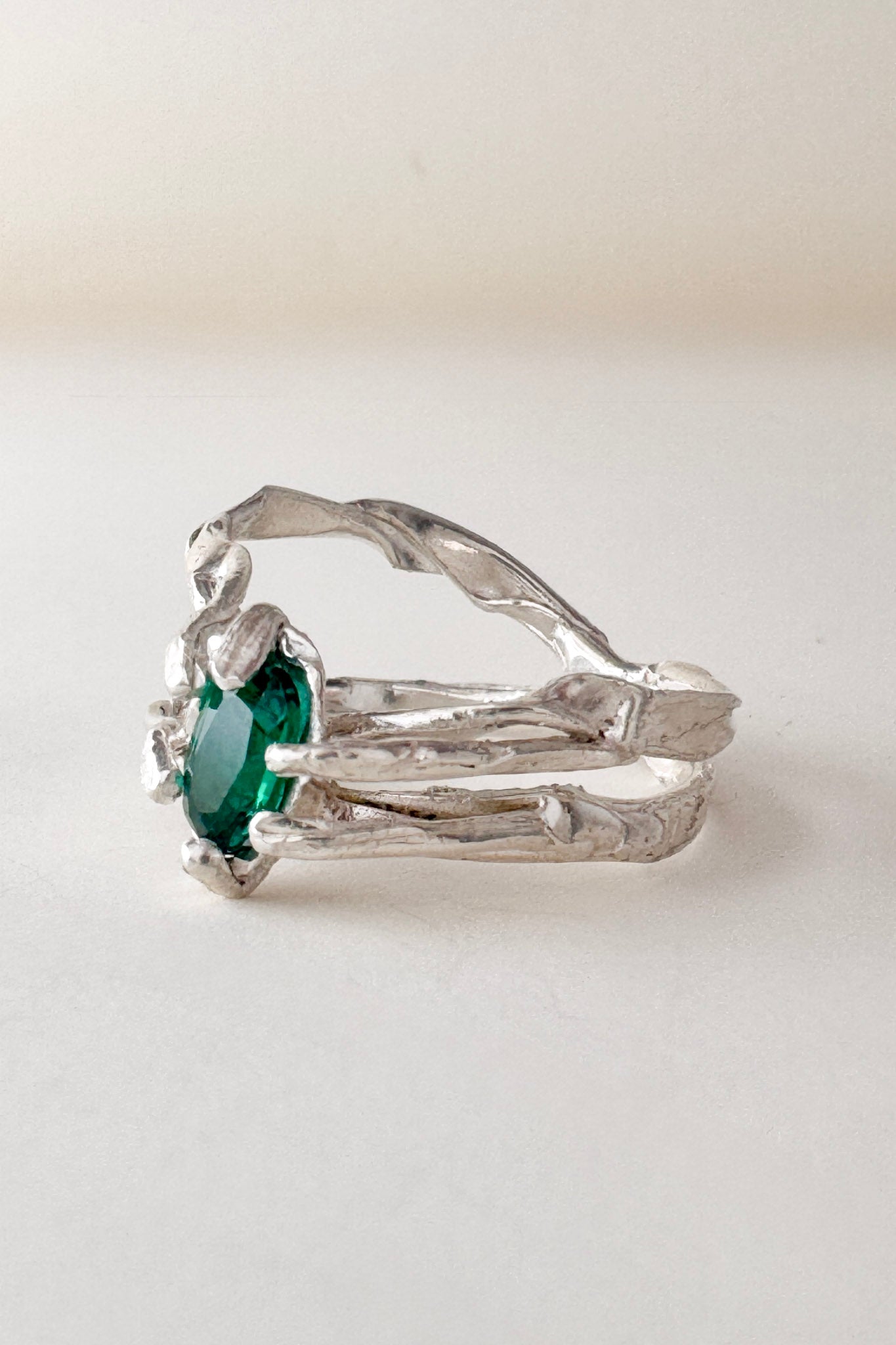 Front-angled view of the sterling silver ring with a vivid green lab-grown emerald, placed on a white surface.