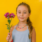 girl with rainbow necklace, holding flowers on a yellow background