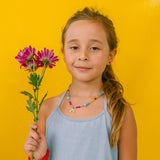 girl with rainbow necklace, holding flowers on a yellow background