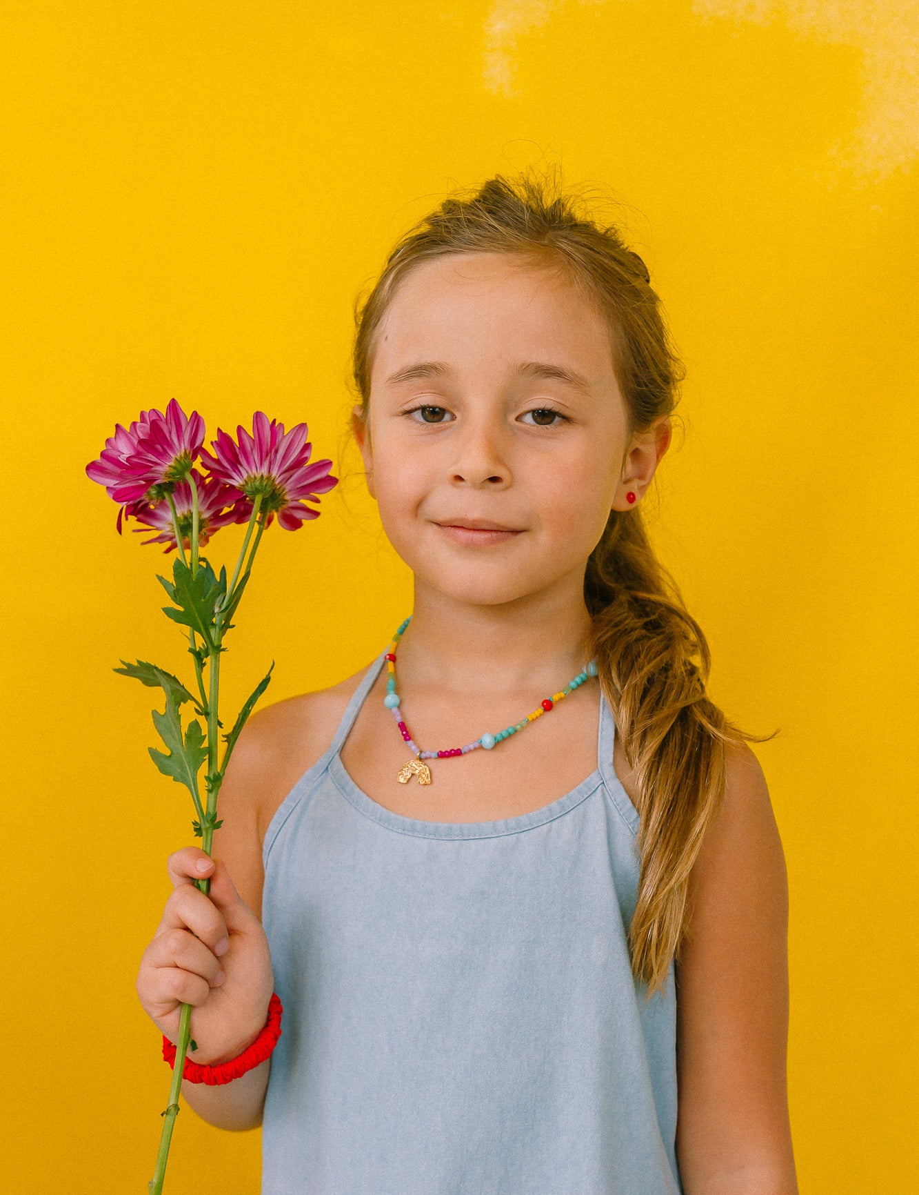girl with rainbow necklace, holding flowers on a yellow background